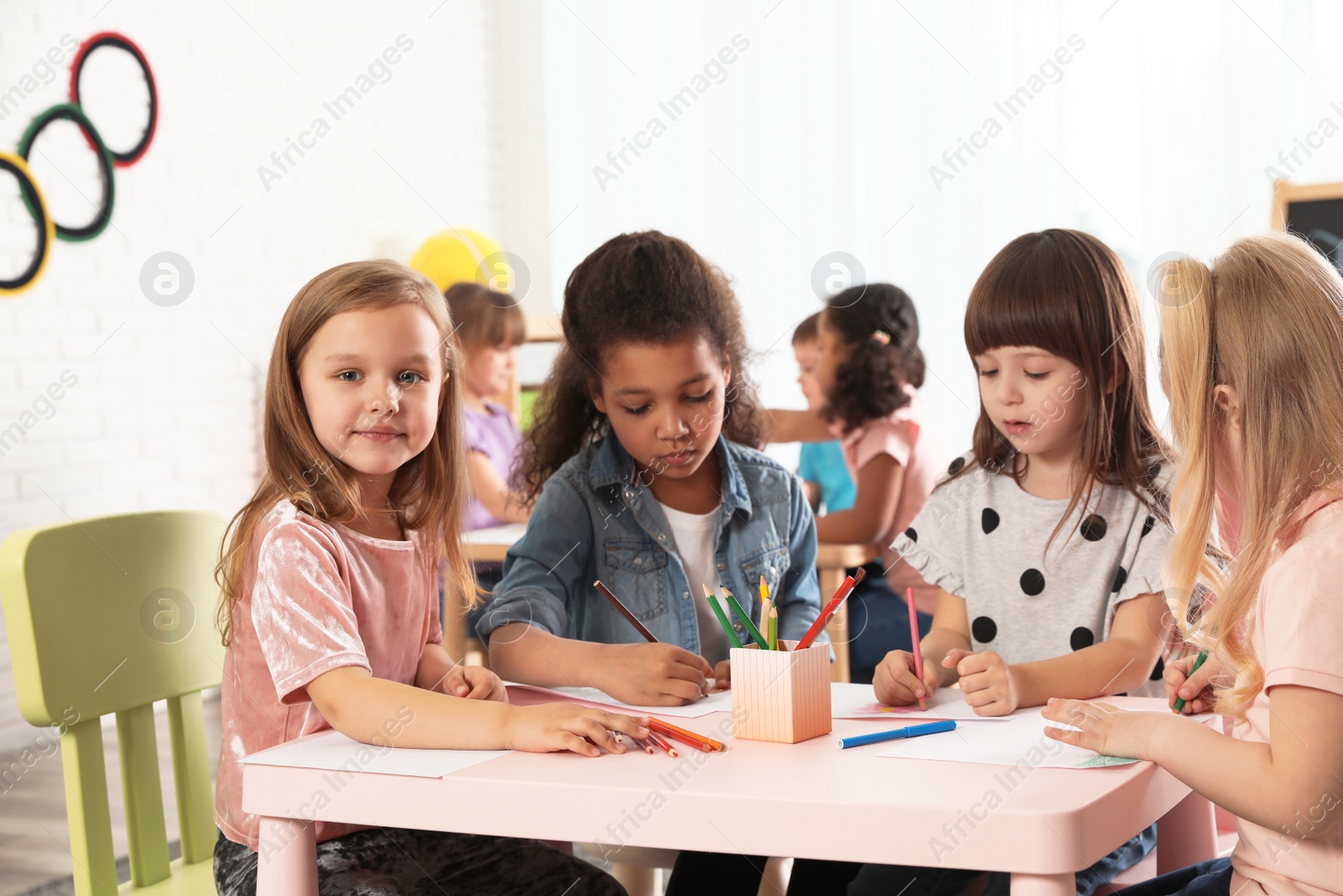 Photo of Adorable children drawing together at table indoors. Kindergarten playtime activities