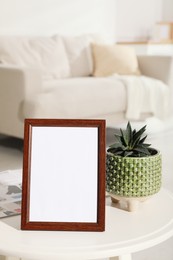 Photo of Empty photo frame, magazine and succulent on white table in living room