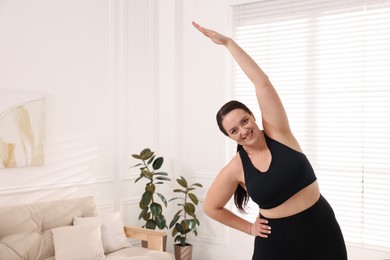 Overweight woman stretching at home, space for text