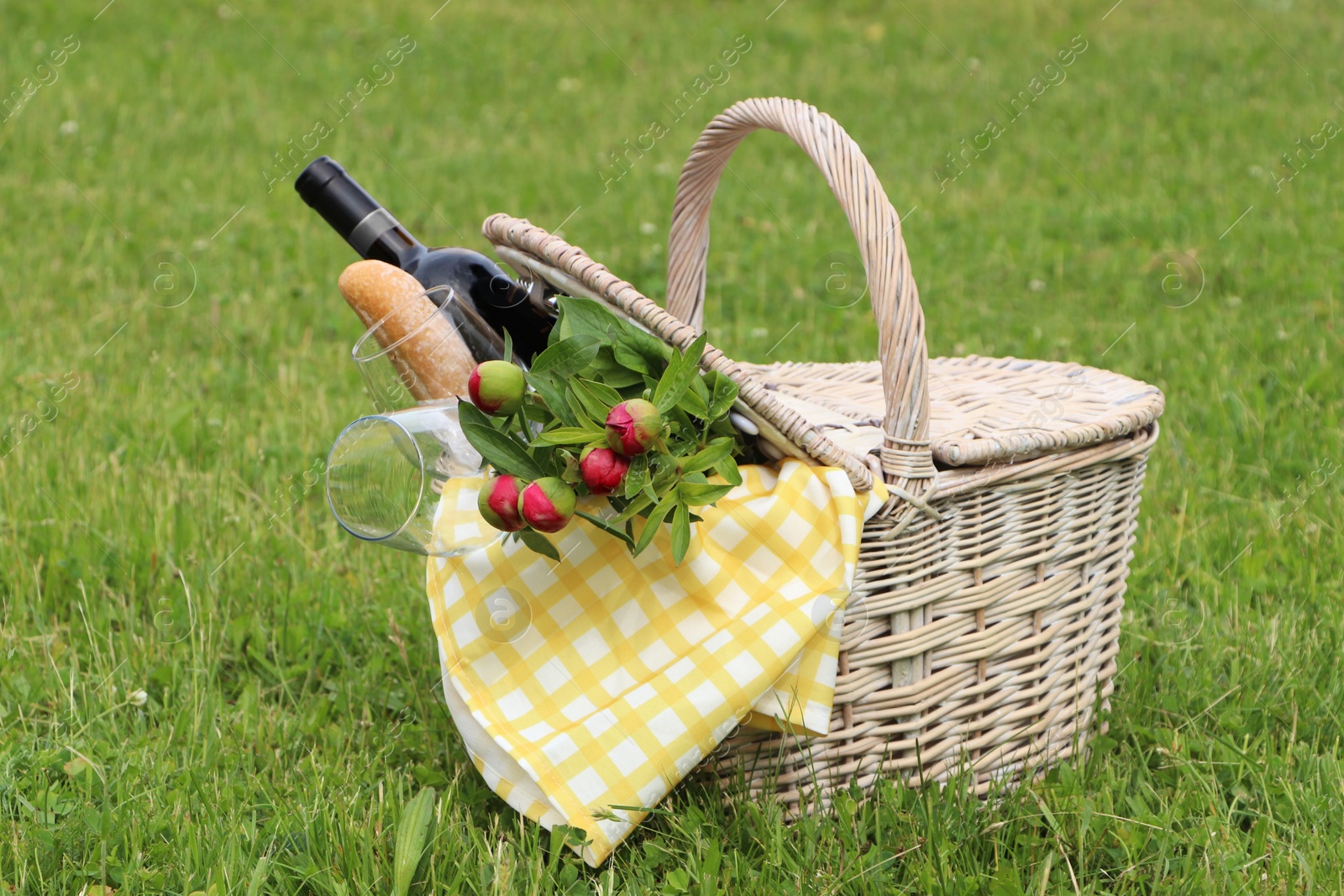 Photo of Picnic basket with wine, bread and flowers on green grass outdoors