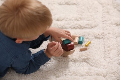 Photo of Little boy playing with wooden balance toy on carpet indoors