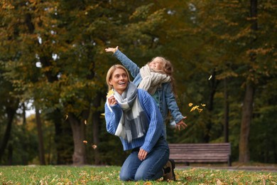 Photo of Happy mother and her daughter playing with dry leaves on grass in autumn park
