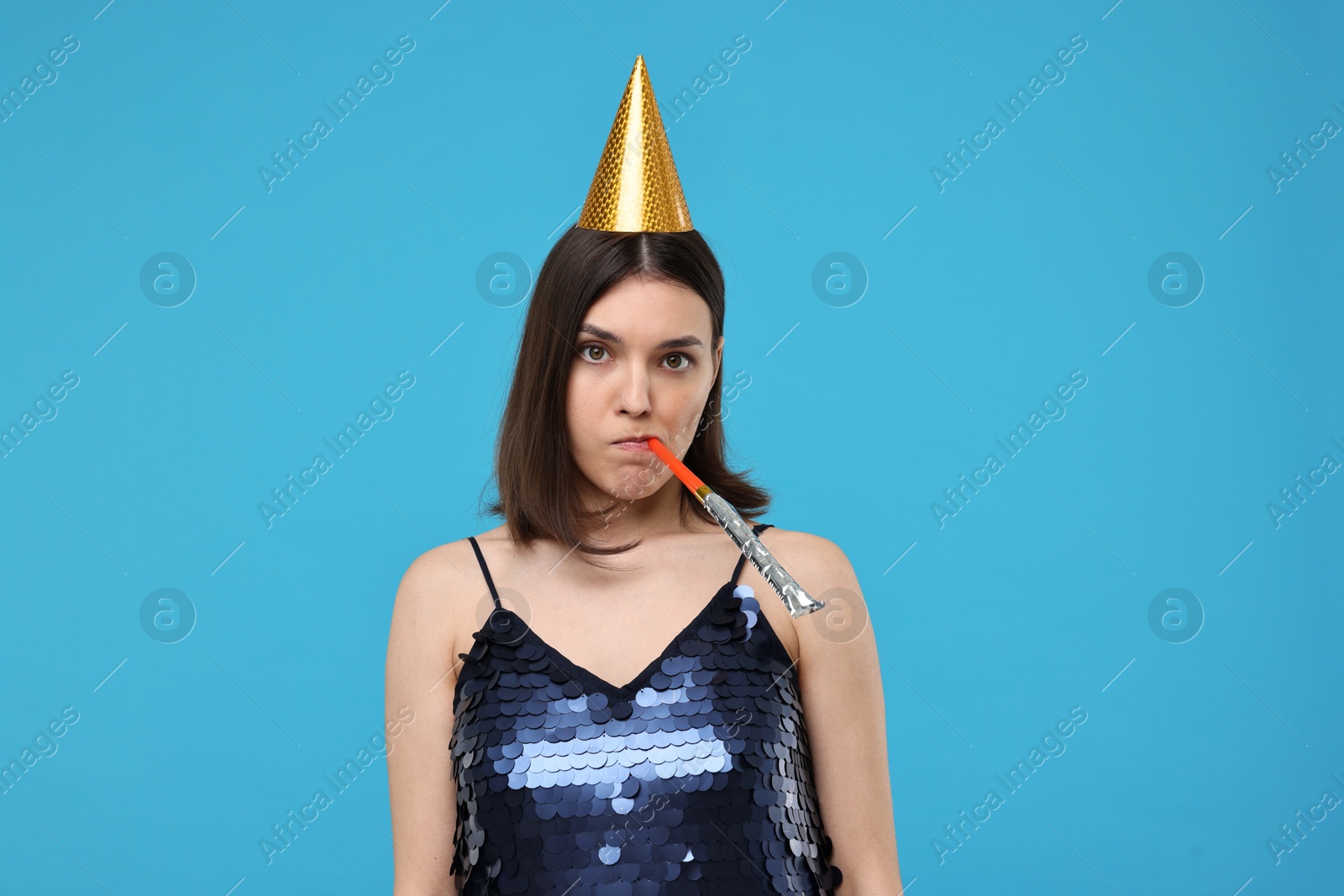 Photo of Sad young woman in party hat with blower on light blue background