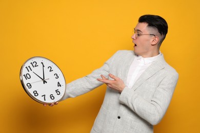 Emotional young man showing clock on orange background. Being late concept