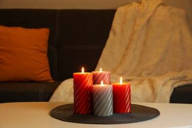 Photo of Burning candles on white table indoors. Cosy atmosphere