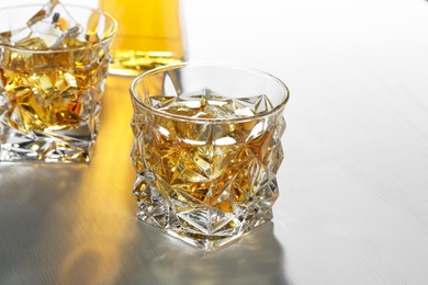 Photo of Whiskey with ice cubes in glasses on white table, closeup