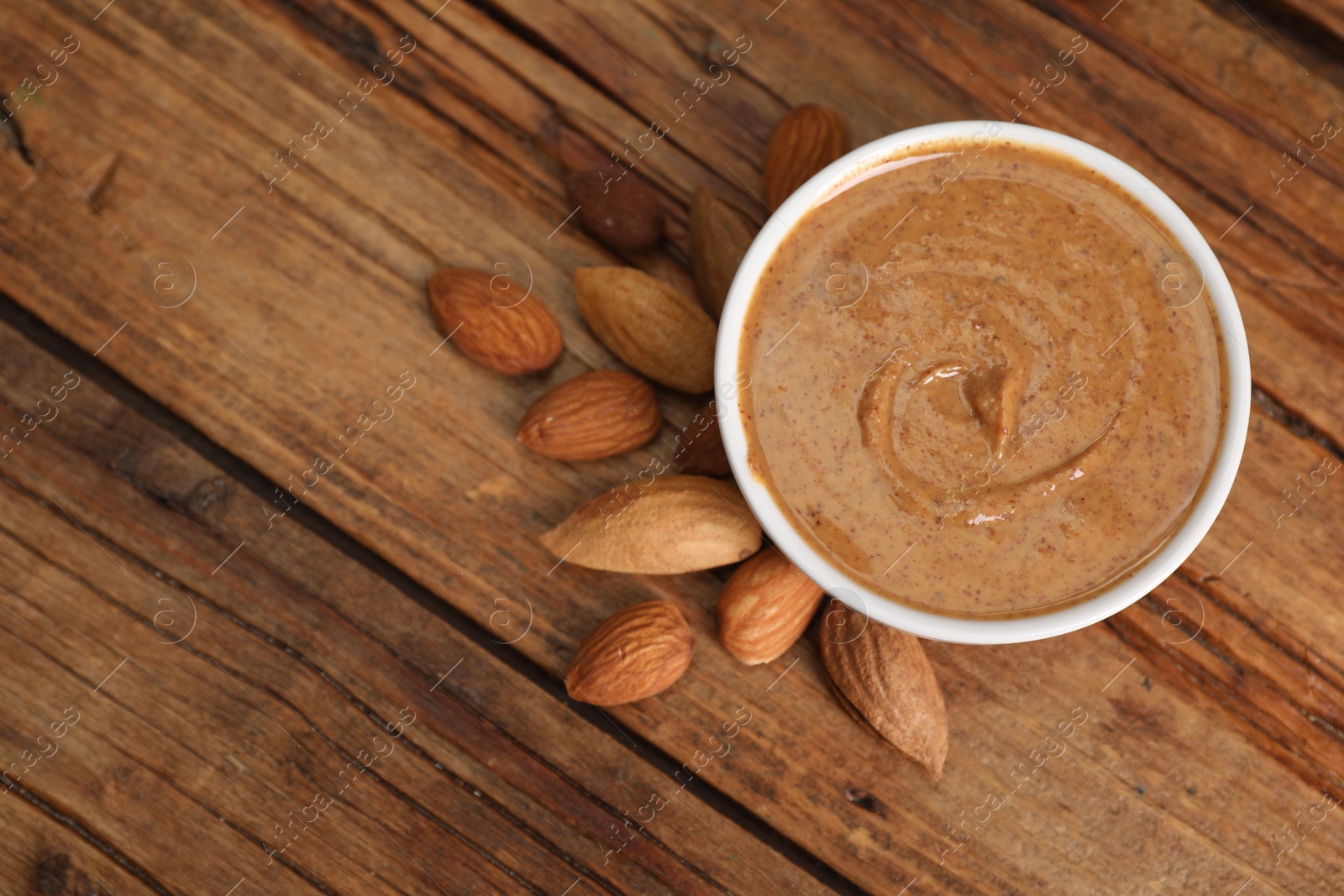 Photo of Delicious nut butter in bowl and almonds on wooden table, top view. Space for text