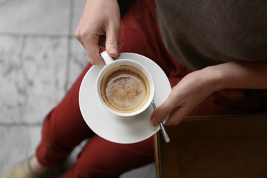 Photo of Young woman with cup of delicious coffee, top view