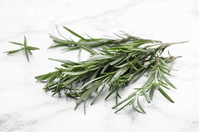 Photo of Sprigs of rosemary on white marble table, closeup
