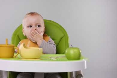 Photo of Cute little baby eating healthy food in high chair on gray background, space for text