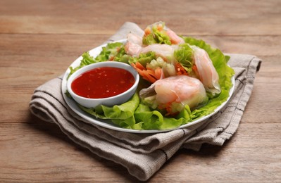 Photo of Tasty spring rolls served with lettuce and sauce on wooden table