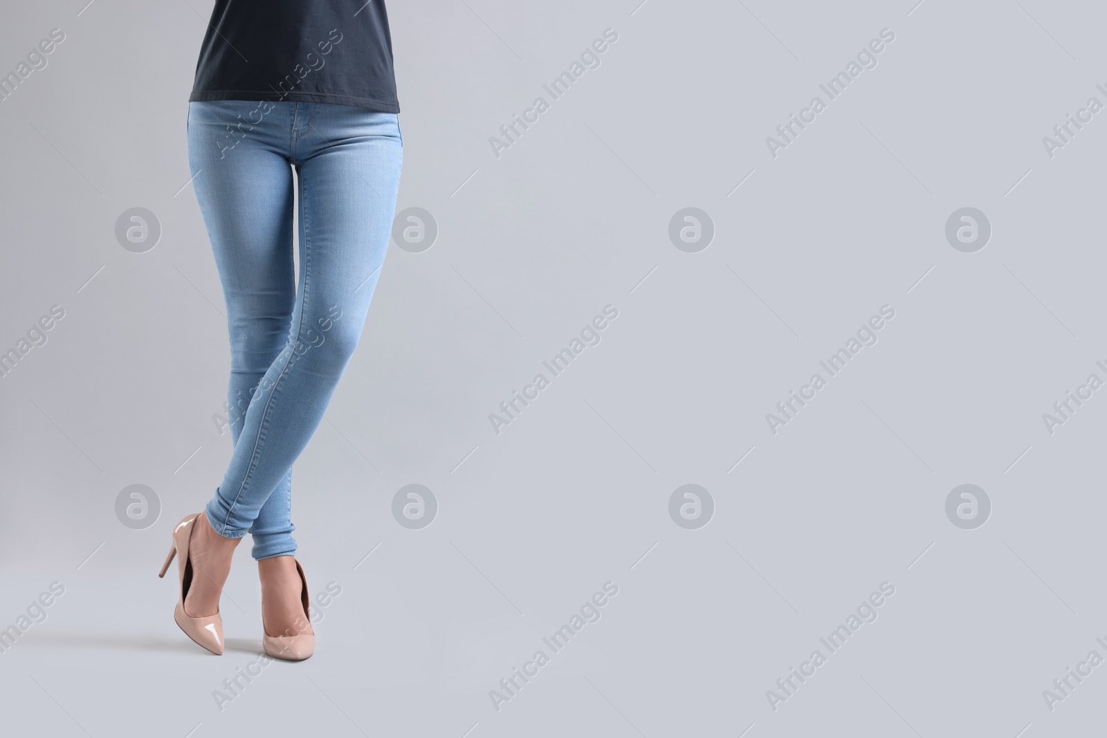 Photo of Woman wearing stylish jeans and high heels shoes on light gray background, closeup. Space for text