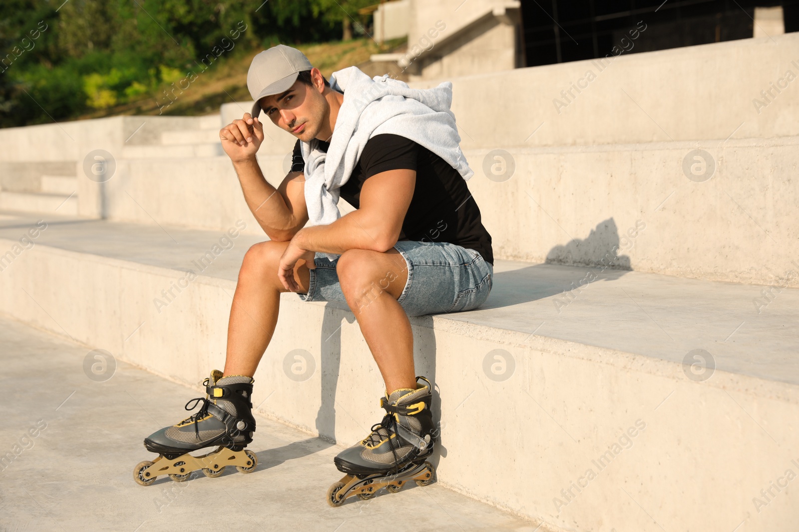 Photo of Handsome young man with inline roller skates sitting on stairs outdoors