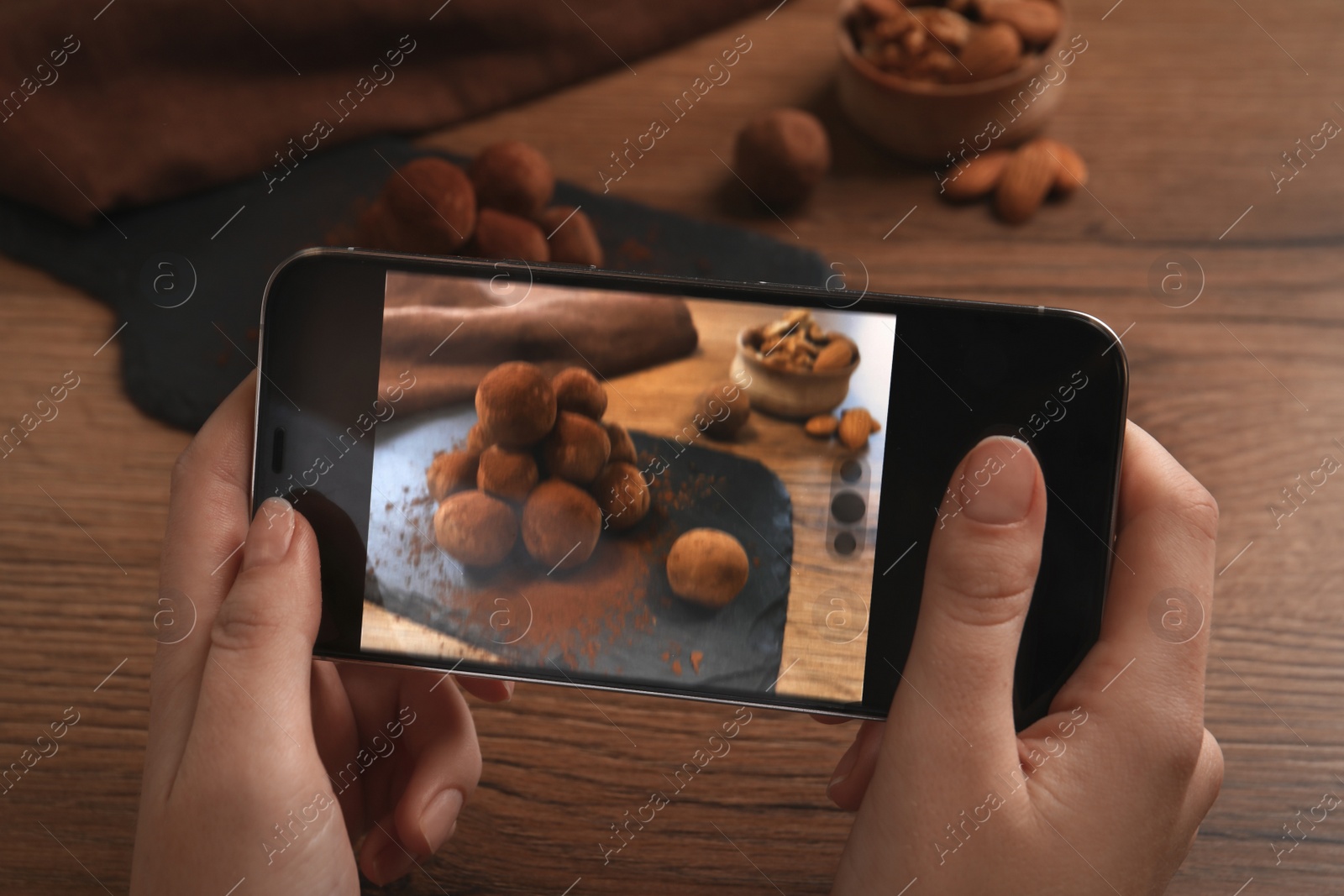 Photo of Woman taking photo of tasty chocolate truffles served on wooden table, closeup