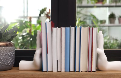 Beautiful hand shaped bookends with books on window sill indoors