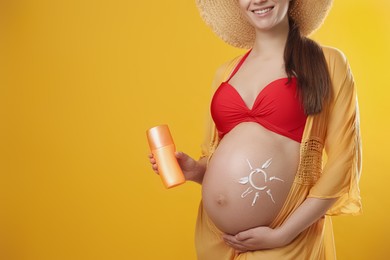 Photo of Young pregnant woman with sun protection spray on yellow background, closeup. Space for text
