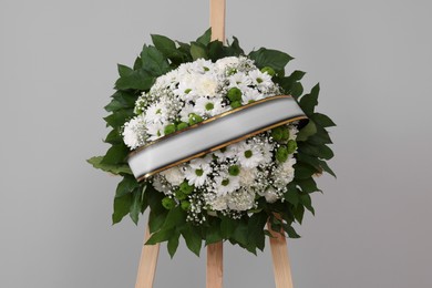 Photo of Funeral wreath of flowers with ribbon on wooden stand against grey background