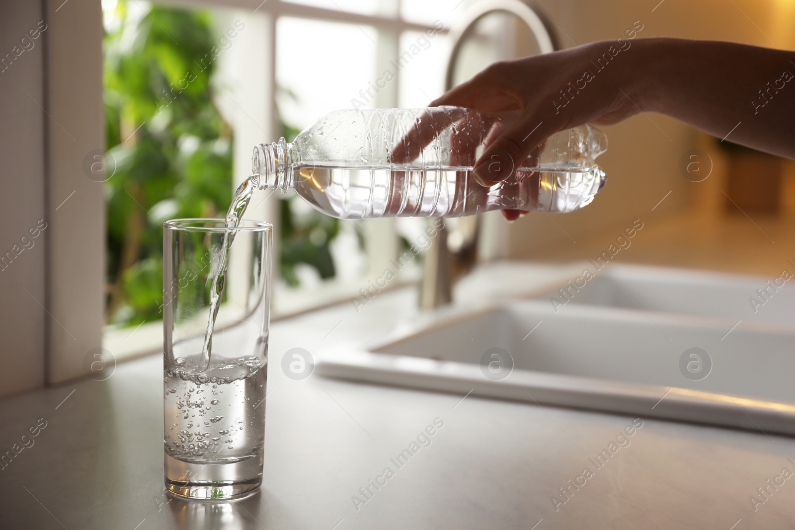 Photo of Woman pouring water from bottle into glass in kitchen, closeup