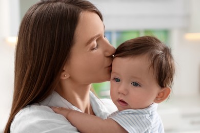 Photo of Happy mother kissing her little baby indoors, closeup