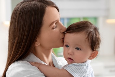 Happy mother kissing her little baby indoors, closeup