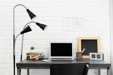 Stylish workplace with laptop on table near brick wall