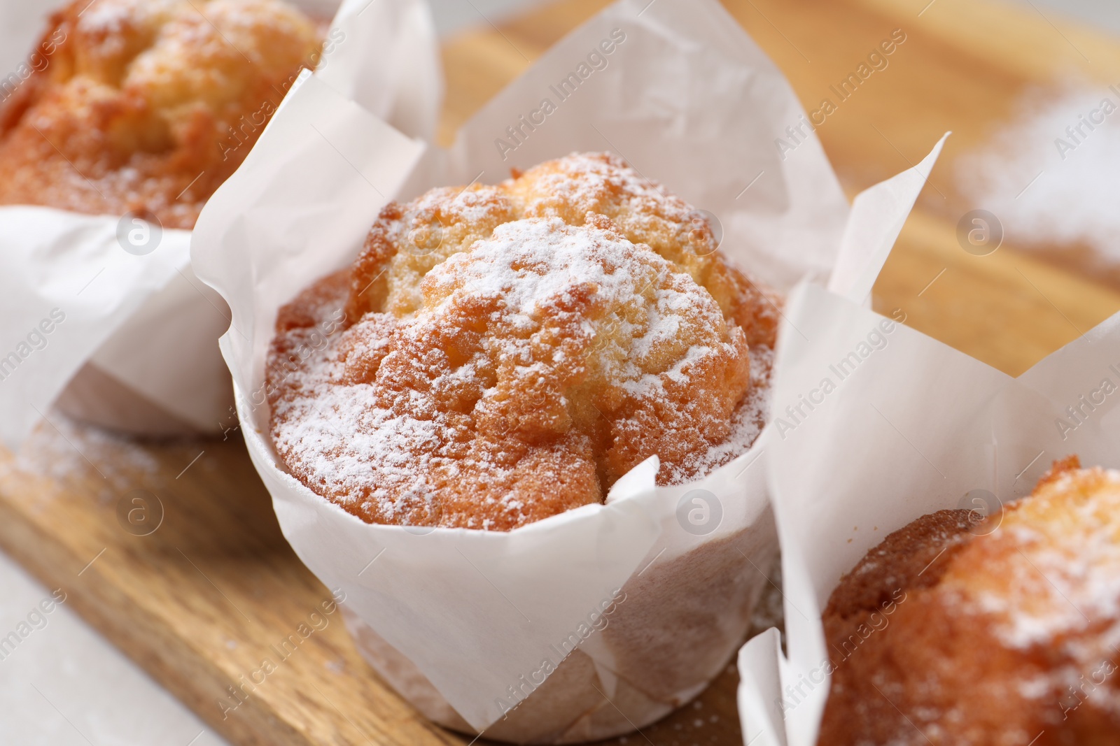 Photo of Delicious muffins with powdered sugar on wooden board, closeup