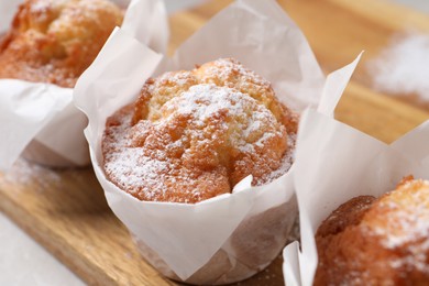 Delicious muffins with powdered sugar on wooden board, closeup