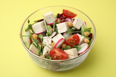 Photo of Bowl of tasty salad with tofu and vegetables on yellow background, closeup