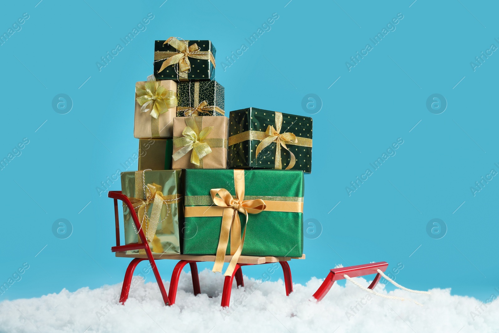 Photo of Sleigh with Christmas gift boxes and artificial snow on light blue background