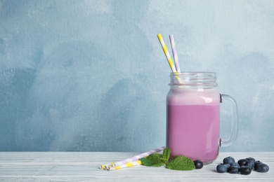 Photo of Mason jar of tasty milk shake and blueberries on table. Space for text