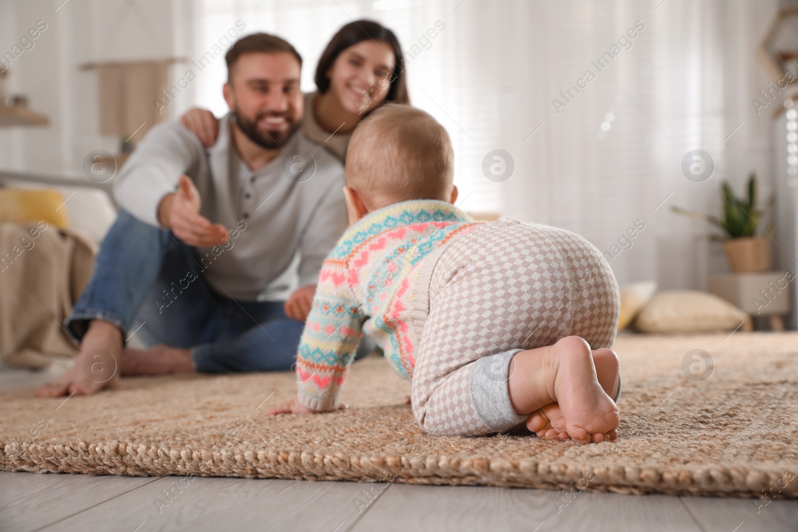 Photo of Happy parents watching their baby crawl on floor at home