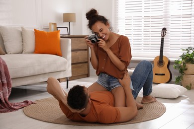 Beautiful African-American woman taking picture of her boyfriend on floor at home