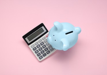 Calculator and piggy bank on pink background, top view