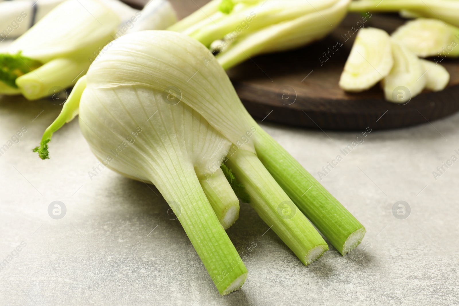 Photo of Whole and cut fennel bulb on light gray table, closeup
