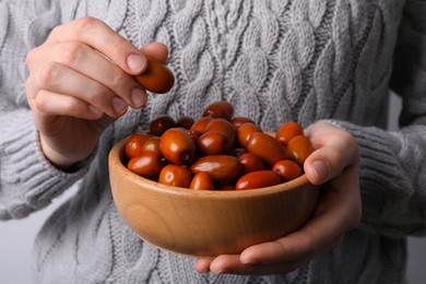 Photo of Woman holding wooden bowl with fresh Ziziphus jujuba fruits on light background, closeup