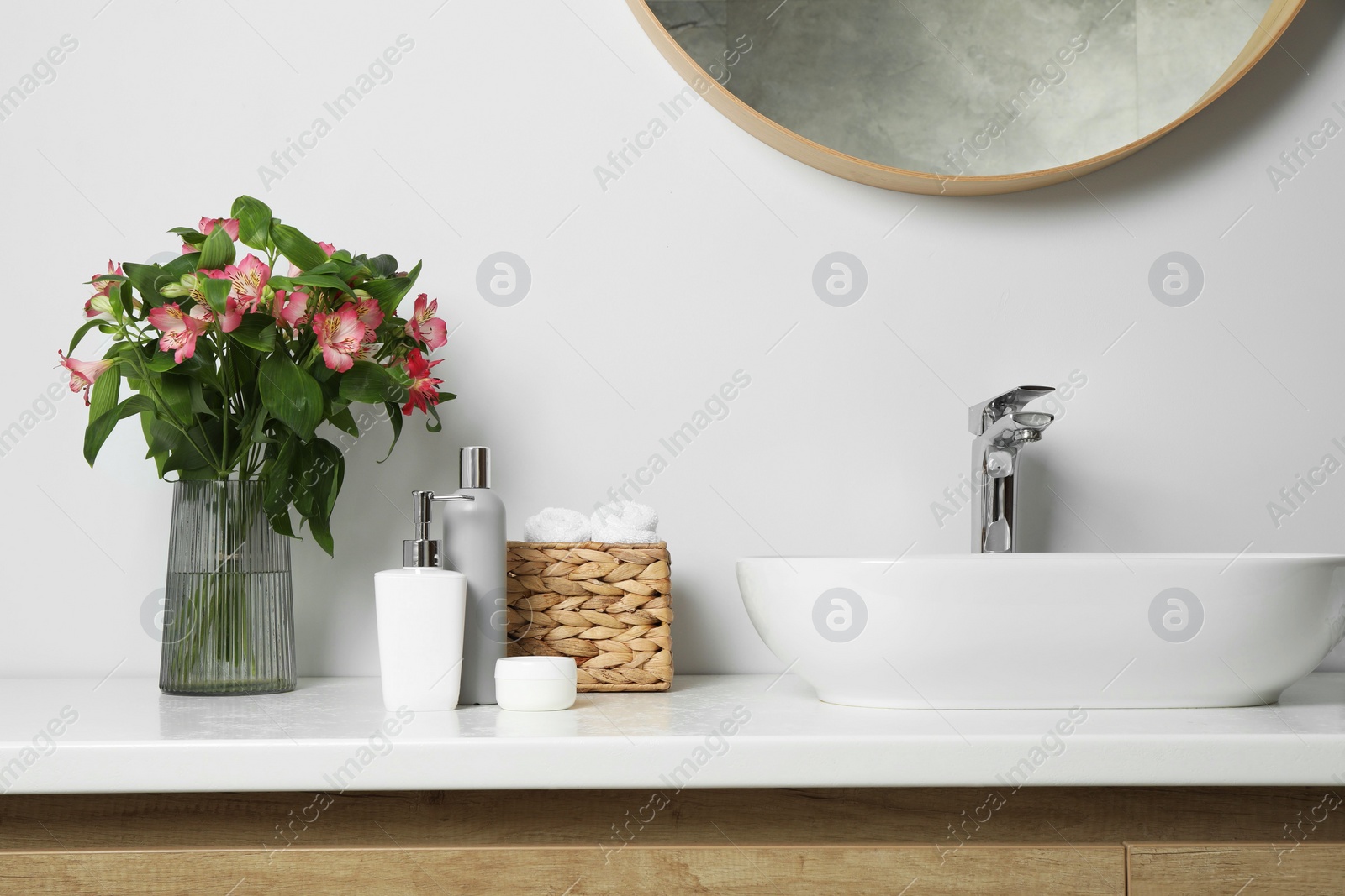 Photo of Vase with beautiful Alstroemeria flowers and toiletries near sink in bathroom