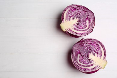 Photo of Halves of ripe red cabbage on white wooden table, flat lay. Space for text