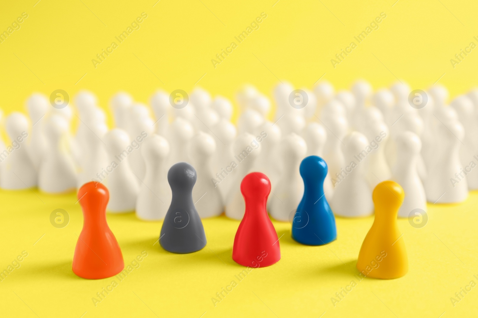 Photo of Colorful pawns on yellow background, closeup. Social inclusion concept