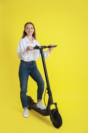 Happy woman with modern electric kick scooter on yellow background