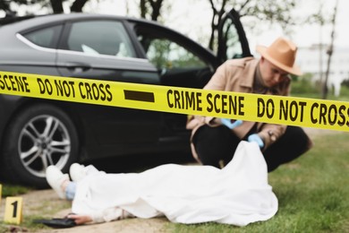 Photo of Investigator working at crime scene with dead body outdoors, focus on yellow tape
