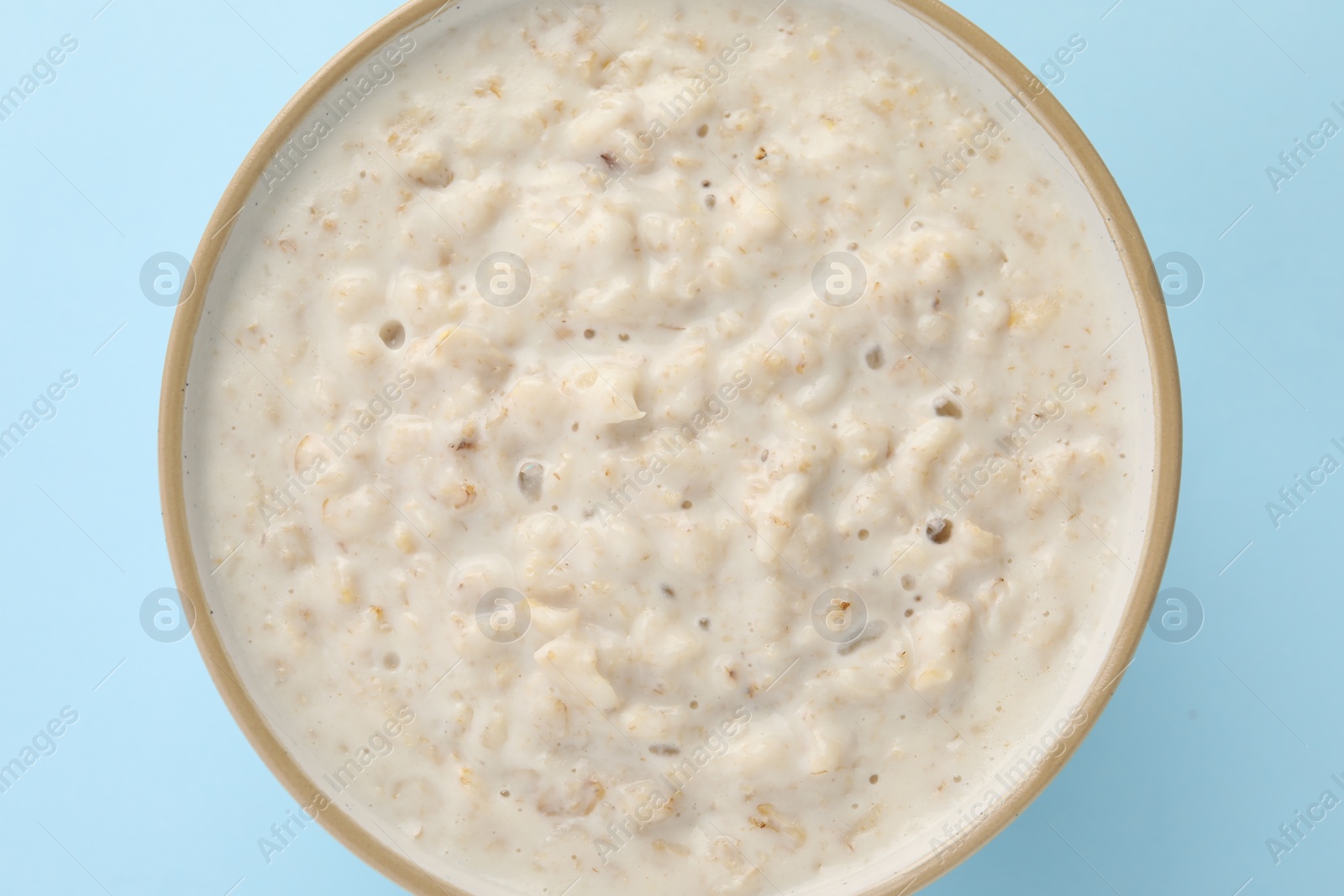 Photo of Tasty boiled oatmeal in bowl on light blue table, top view