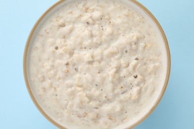 Photo of Tasty boiled oatmeal in bowl on light blue table, top view