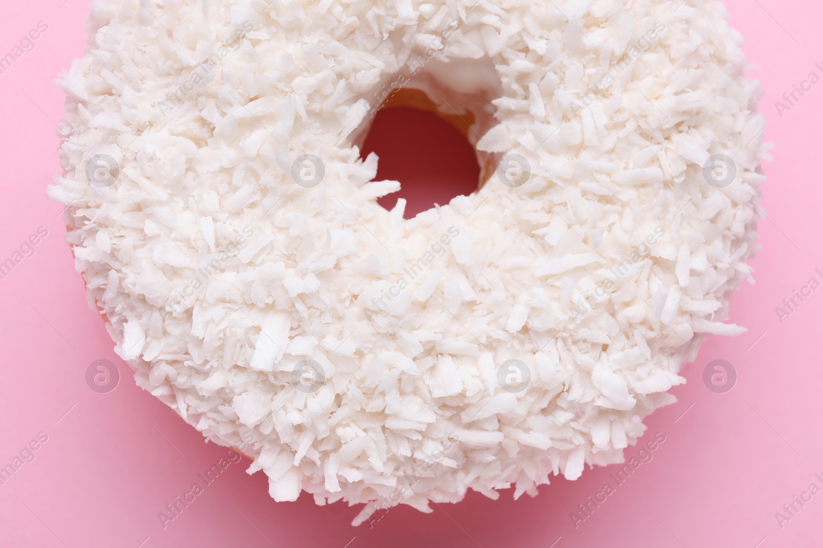 Photo of Tasty glazed donut with coconut shavings on pink background, closeup