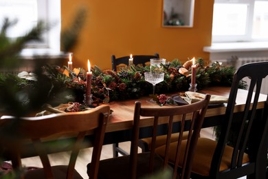 Dining table with burning candles and Christmas decor in stylish room. Interior design