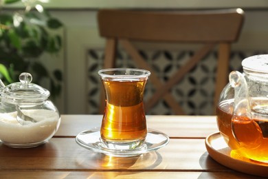 Photo of Aromatic tea in glass, teapot and sugar on wooden table indoors