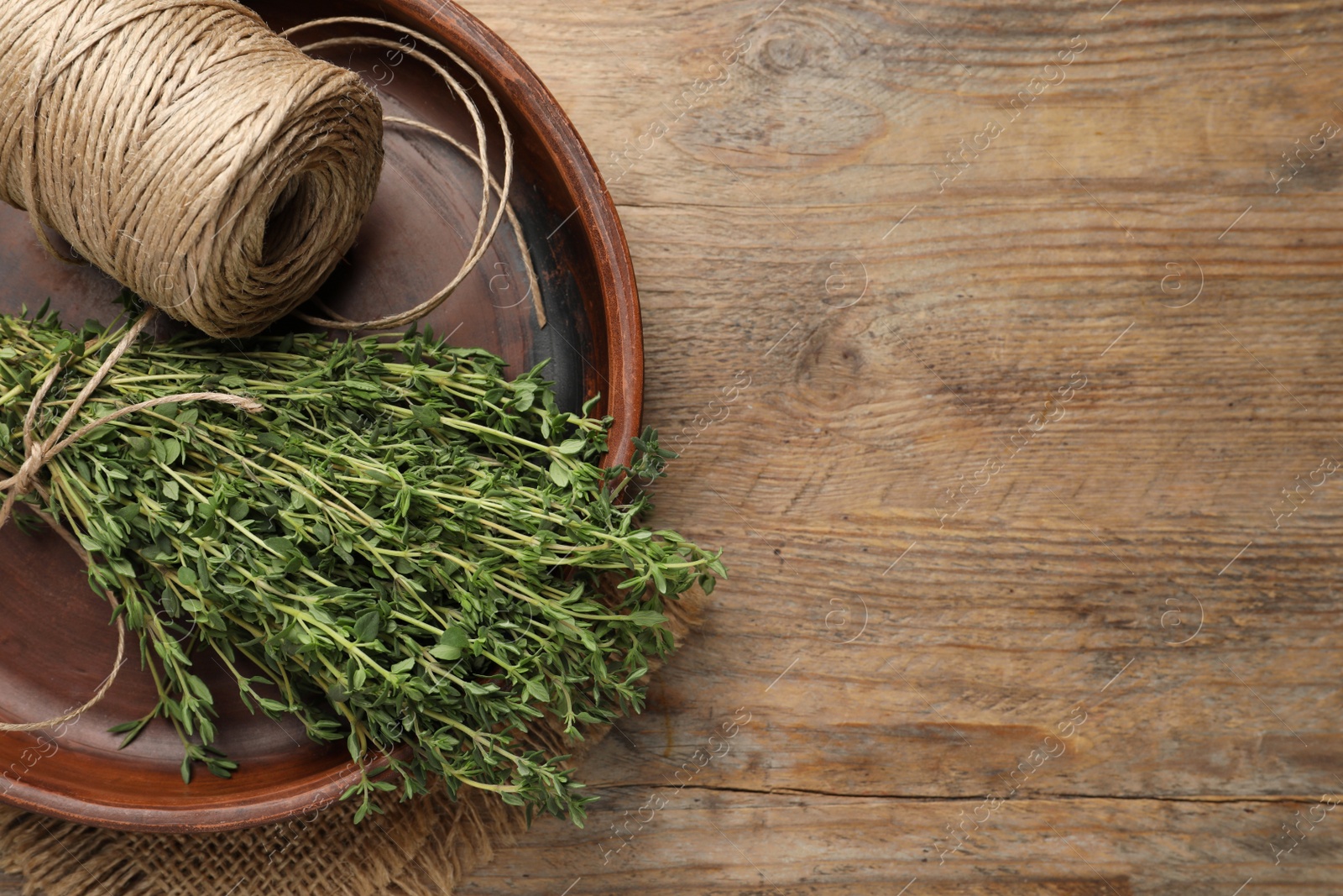 Photo of Bunch of aromatic thyme and twine in bowl on wooden table, top view. Space for text