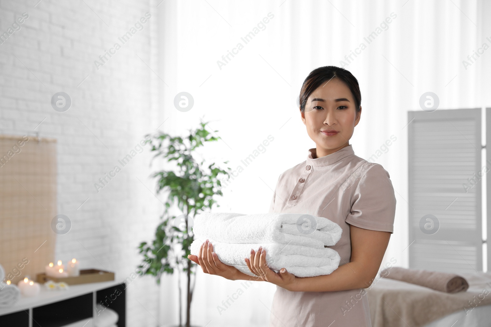 Photo of Portrait of young Asian masseuse with towels in spa salon. Space for text