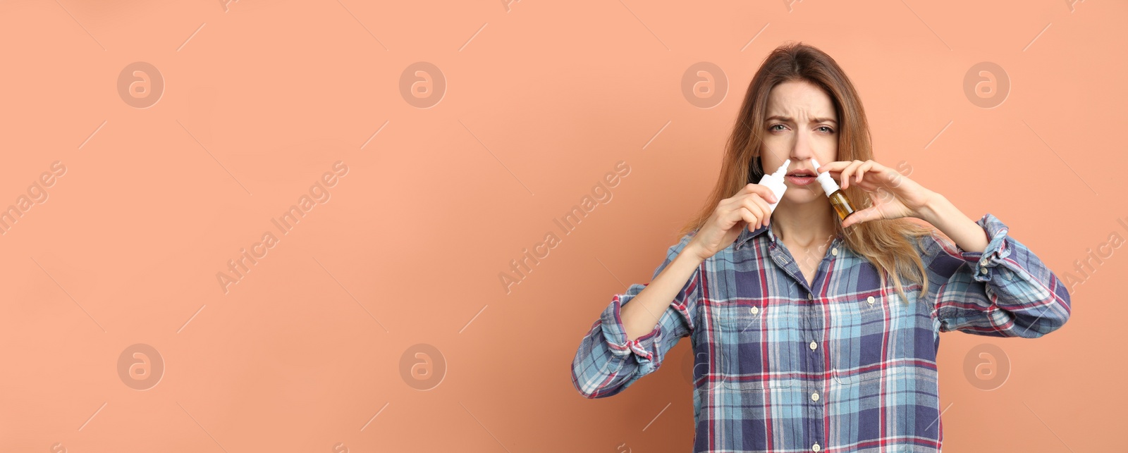 Photo of Sick young woman using nasal sprays on coral background