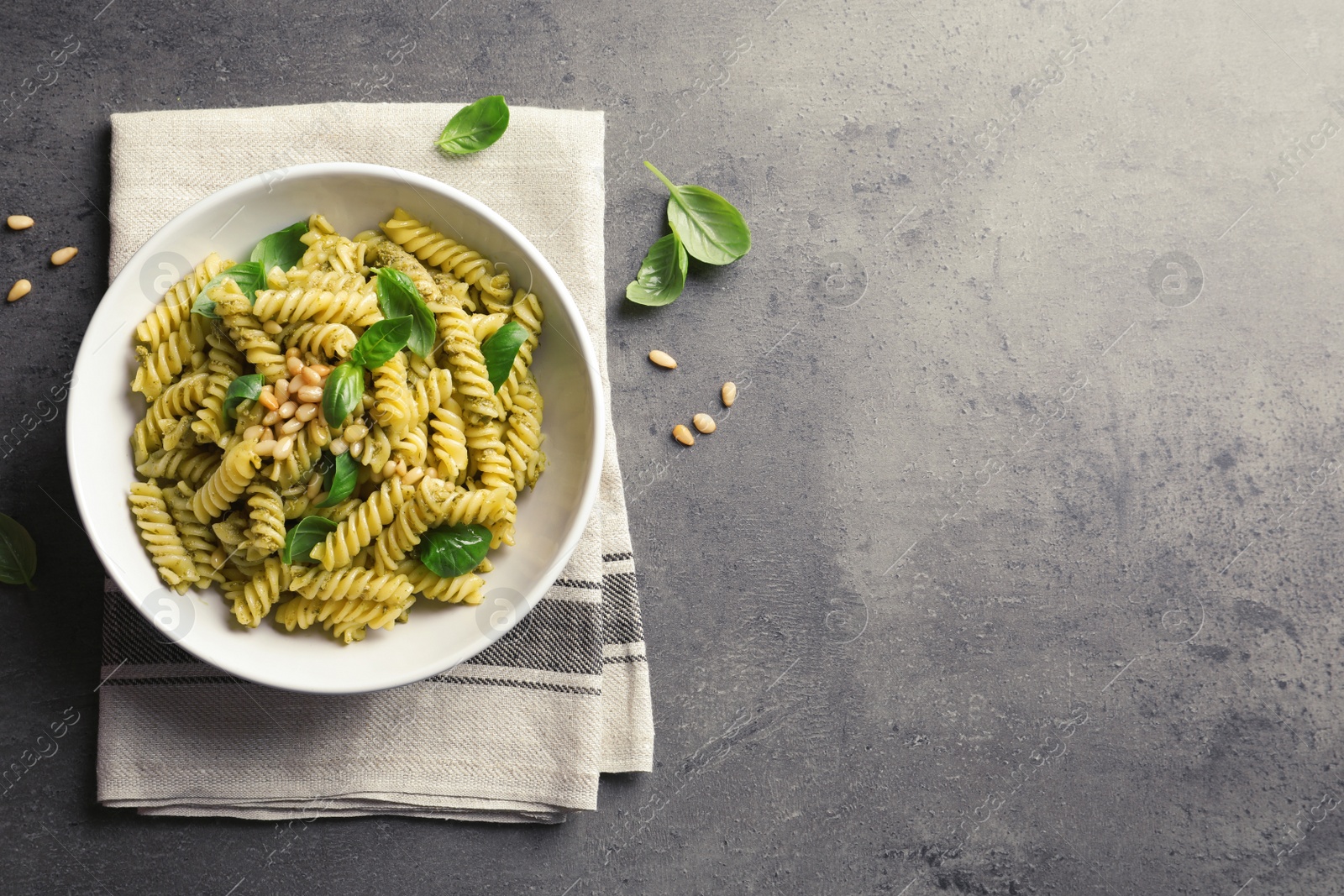 Photo of Plate of delicious basil pesto pasta on gray table, top view. Space for text