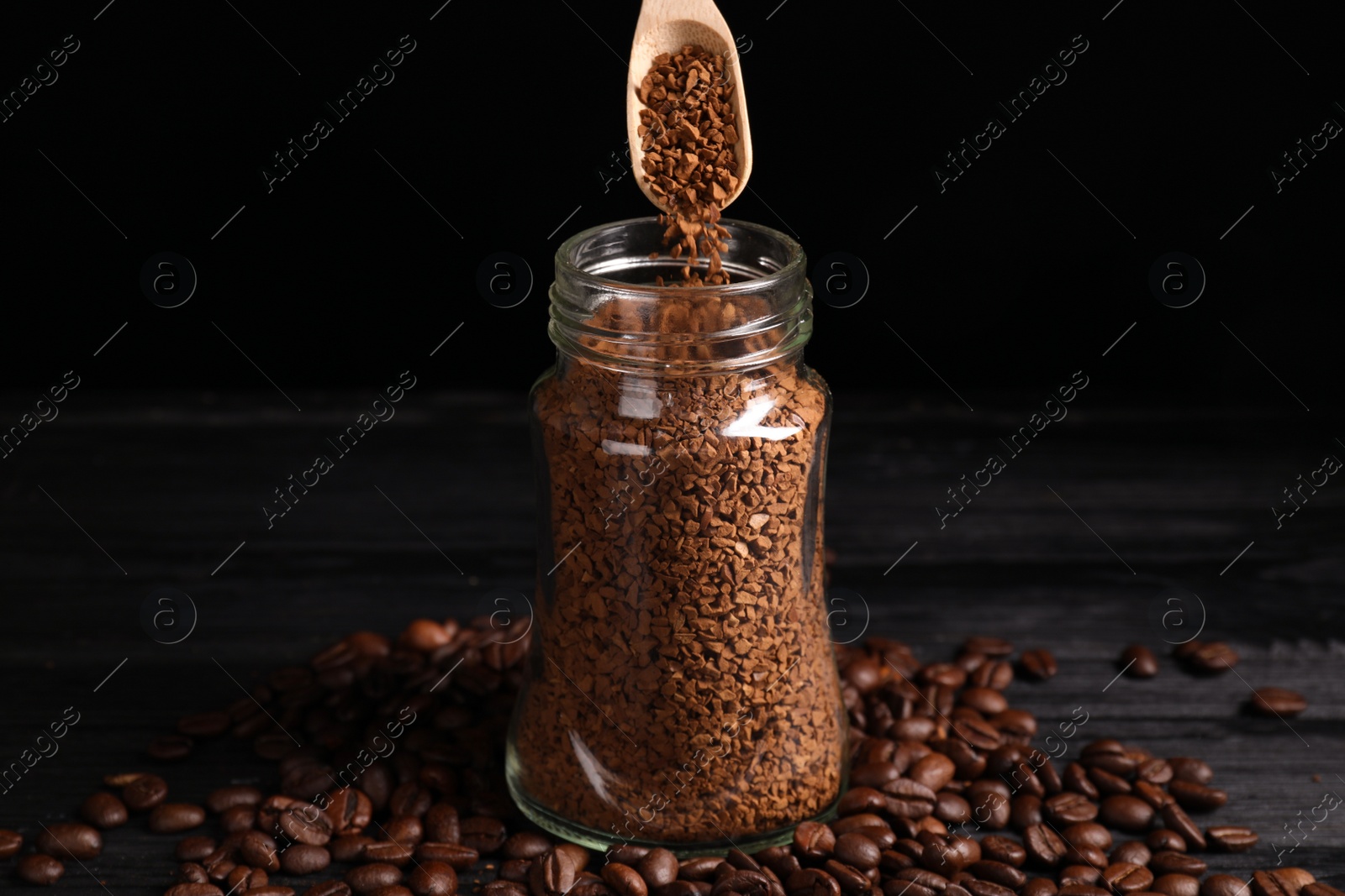 Photo of Putting instant coffee into glass jar on black wooden table